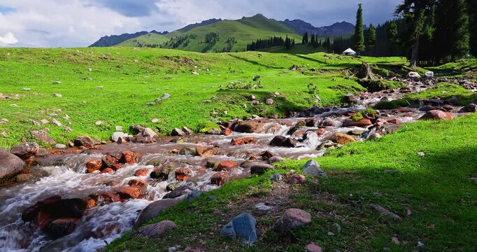 Beautiful Nalati grassland scenery in summer. Flowing stream and green grassland with mountain natural landscape in Xinjiang. Famous travel destination in China.