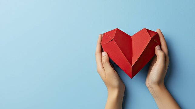 Person holding a vibrant red heart with love and compassion in their hands, symbolizing care and affection in a heartfelt gesture.