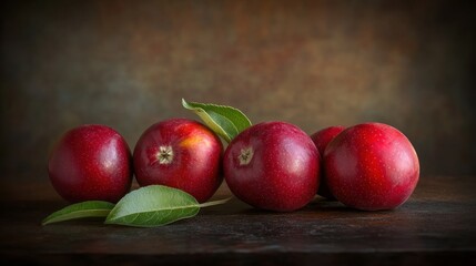 Five ripe red apples with green leaves on rustic wooden surface.