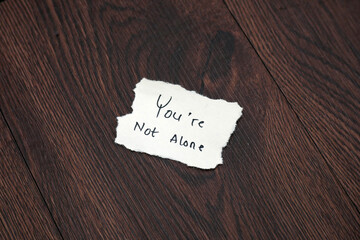 you are not alone handwritten on torn paper on a wooden table