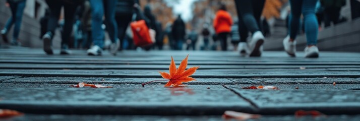 Obraz premium Single autumn leaf on wet pavement with blurred pedestrian background.