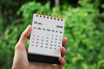 Close-up of a hand holding a monthly desk calendar for January 2025 on a blurry background.