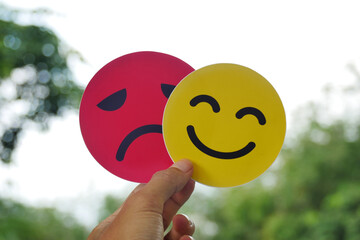 Hand holding a sad face card hiding behind a happy smiling face. Bipolar and depression concept,...