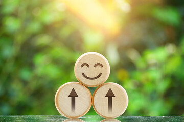 Round wood with carved smiling face and rising arrow. Background is blurred leaves. Positive and optimistic concept, indicating growth and progress of happiness, mental health.