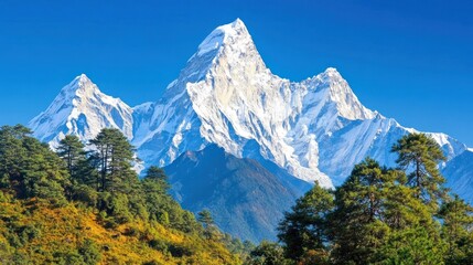 Fototapeta premium Majestic snow-capped mountain peaks rise above a lush green valley under a vibrant blue sky.