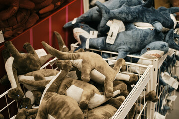 Soft colorful plush toys in the form of animals are sold in a children's toy store. Adorable blue sharks and grey dinosaurs.