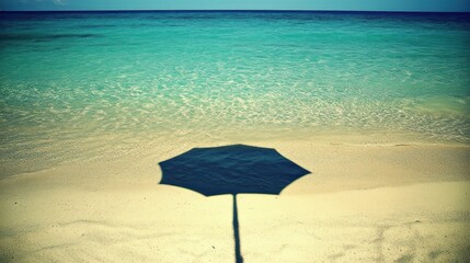 Beach umbrella shadow on tranquil turquoise ocean.