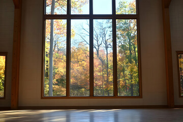 A spacious room with large windows showcasing vibrant autumn foliage outside.