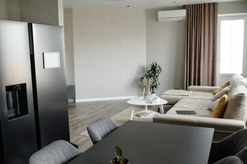 Modern dining area with graphite fridge and same colored table, light living room with comfortable couch and multicolored cushions