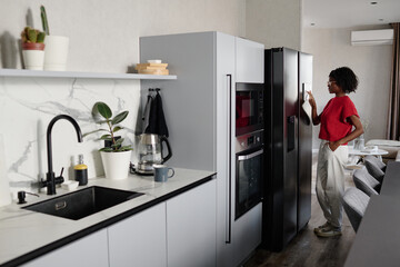 Clean minimalist kitchen area with woman standing next to smart fridge and using control system