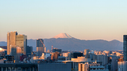 Spectacular view of sacred Mount Fuji from the city of Tokyo, with tokyo city skyline and buildings in the foreground, mt fuji on the horizon line with mountains and clear sky above