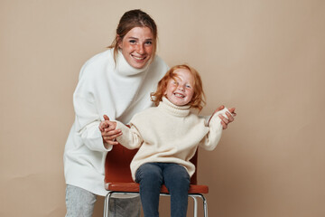 Mother and daughter relaxing on a chair in front of a beige background, family bonding moment,...