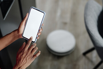 High angle shot of unrecognizable female hands controlling robot vacuum cleaner on app
