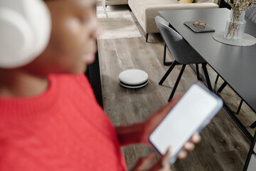Robot Vacuum cleaning parquet while unrecognizable housewife checking progress on app