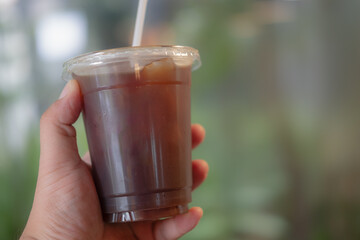 Hand holding ice american coffee in plastic glass with bokeh nature light