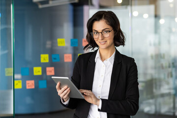 Confident businesswoman using tablet in modern office setting, engaging with tasks efficiently....