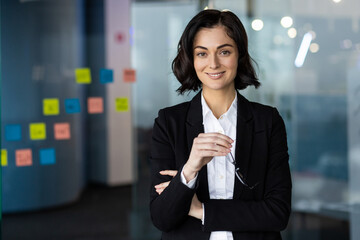 Confident businesswoman in modern office holding glasses, portraying leadership, professionalism,...