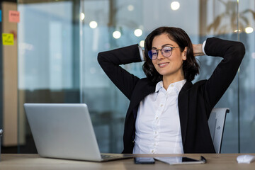 Professional woman relaxing in office after successful work session on laptop. She exudes...
