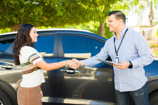 Cheerful driving instructor shaking hands with his teen student after a successful driving test, next to a car