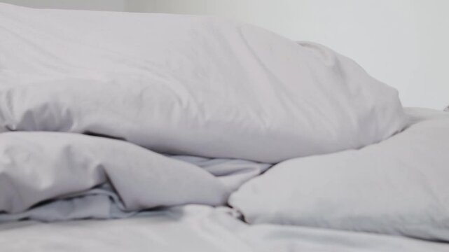 Woman hiding under a blanket in a gray, minimalist room, struggling with depression and emotional distress.