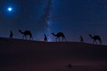 Christmas Jesus birth concept - Adoration of the Magi, Three Wise Men, Three Kings, and the Three biblical Magi with camel silhouettes journeying in sand dunes of desert follow Bethlehem star at night © Dmitry Rukhlenko