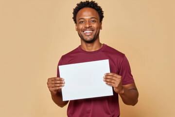 An advertisement studio template portrait photo of a person: an African American man with a bright smile on his face, holding a blank white paper in his hands against a beige background.