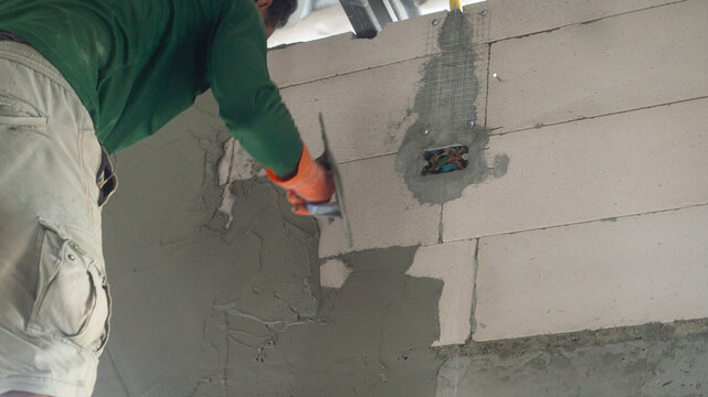 The walls of the house are drilled into embedded blocks for installing air conditioners. A male worker is plastering lightweight bricks with cement. Concept of working in a construction site