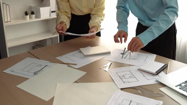 Architect and safety engineer discussion about building blueprint displaying on laptop on table with architectural document and wooden block scatter around at modern office. Closeup. Delineation.