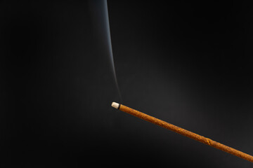Incense, aroma stick smoldering with puffs of smoke on black background, close-up.