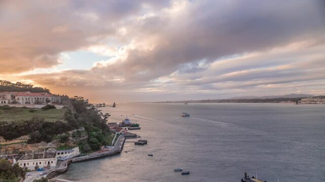 Aerial timelapse panorama from a hill near Porto Brandao Ferry Station on the Tagus River in Lisbon. Dramatic sunset with colorful clouds, a ship floating on water and Terminal in background
