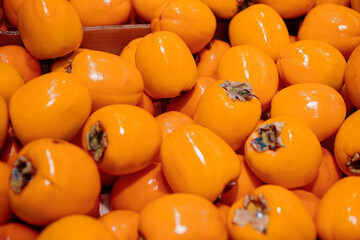 Pile of bright persimmons, a type of fruit, with some green leaves still attached to their tops. Persimmons are closely packed together, creating a vibrant and colorful display
