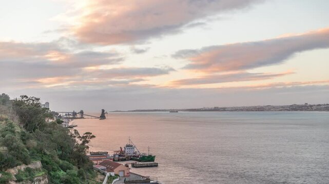 Aerial timelapse from a hill near Porto Brandao Ferry Station on the Tagus River in Lisbon. Dramatic sunset with colorful clouds, a ship floating on water and Terminal Portuario Trafaria in background