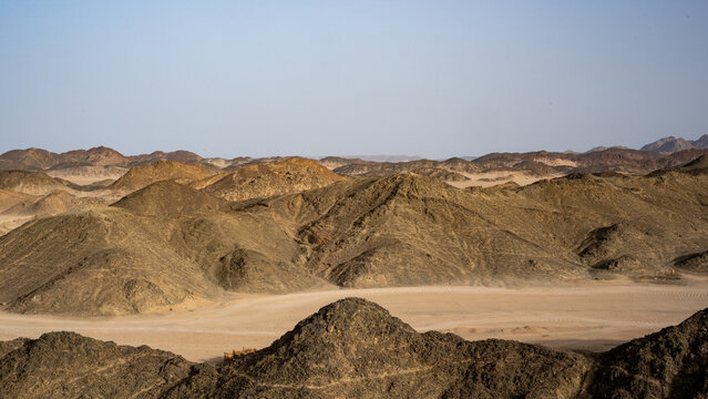 Majestic Desert Landscape: A Vivid Display of Rocky Hills, Arid Terrain, and Barren Sandy Surfaces Under a Clear Blue Sky, Showcasing the Stark Beauty and Solitude of Nature's Rugged Wilderness