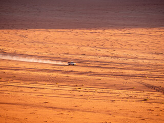 Car speeding through the vastness of the desert in Wadi Rum, Jordan during sunset
