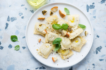 Plate of ravioli with cheese and fresh basil, horizontal shot on a white and blue granite background, elevated view