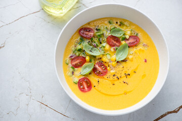 Chilled gazpacho with sweet corn and yellow tomatoes, horizontal shot on a white granite background, high angle view