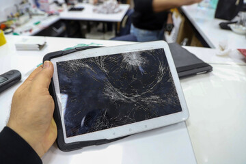 A hand holding a tablet with a severely cracked screen, emphasizing the damaged display in the foreground. © ismailbasdas