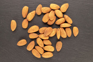 Fragrant roasted almonds with kitchen utensils on slate stone, close-up, top view.
