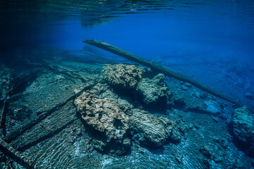 Sunken logs with rocks underwater in crystal blue lake with fresh water
