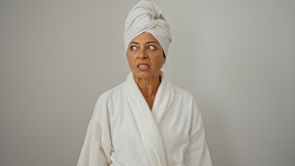 Woman wearing bathrobe and towel with a surprised expression isolated on a white background, mature brunette displaying unusual reaction, hispanic female in spa attire