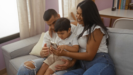 Hispanic family of man, woman, and child sitting together on a couch in a living room, deeply...