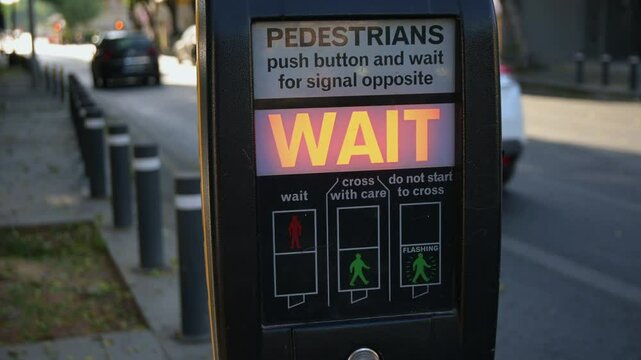 A pedestrian presses the button on an electronic traffic light to cross a busy street in central Nicosia, Cyprus. Wait sign lights up, symbolizing modern traffic safety systems