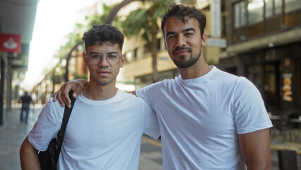 Men standing together on an urban street, showing family love and unity in an outdoor city setting, both wearing white t-shirts, one with glasses