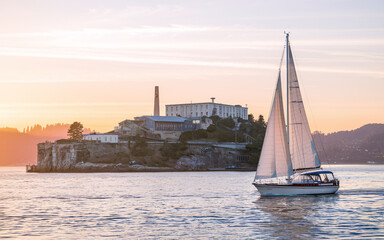 Sailboat sailing past Alcatraz Island at sunset.