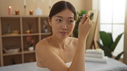 Woman relaxes in a serene spa room using a jade roller on her face, surrounded by soft lighting and cozy decor, emphasizing wellness, relaxation, and self-care in a beautiful setting