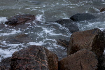 Sea waves are circling in large boulders near the shore