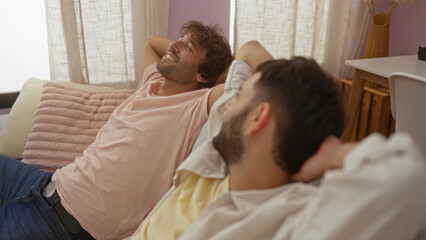 Obraz premium Men relaxing on a living room couch, enjoying a moment of laughter, showcasing their close friendship in a cozy home environment
