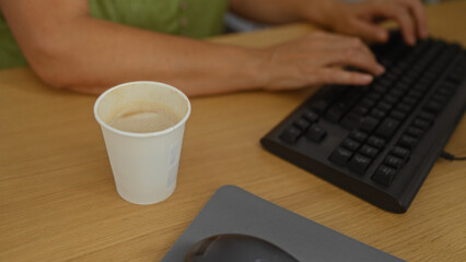 Woman typing on keyboard with coffee cup at desk in office setting implying work or break time...