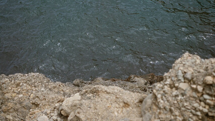 Rocky shore meeting calm ocean water with visible textures of gray rocks and blue waves
