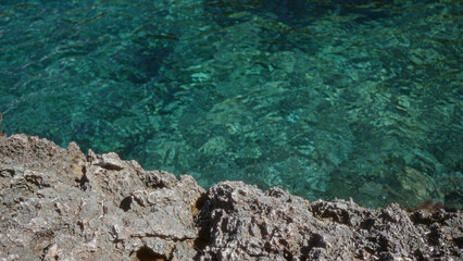 Clear turquoise water along rocky coastline in mallorca, spain featuring textured rocks and beautiful seascape.